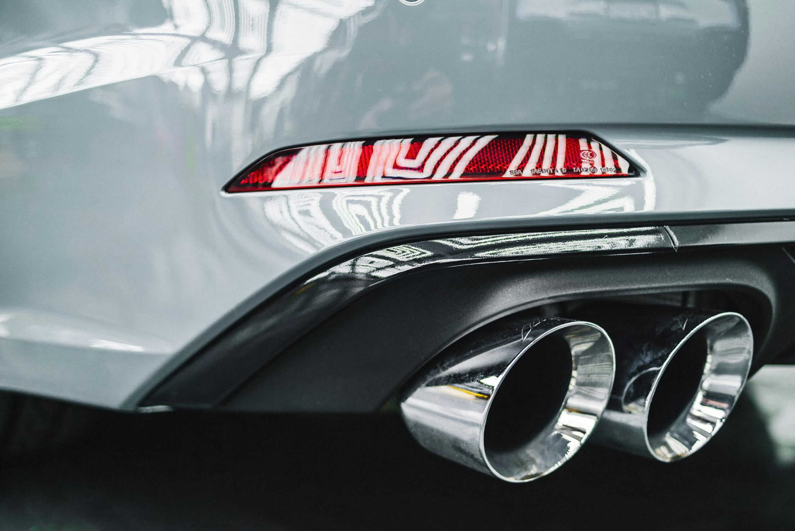 Detailed view of a car's exhaust pipes and rear taillight with reflections.